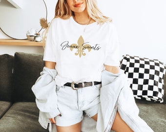 Könnte beinhalten: Weißes T-Shirt mit einer goldenen Fleur-de-lis und dem Text "Geaux Saints" in Schwarz.