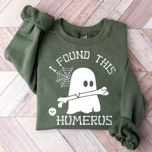 May include: Green sweatshirt with a white ghost holding a bone and the text "I found this humerus".