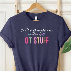 May include: A navy blue t-shirt with the text "Can't talk right now Doing OT STUFF" in white and colorful letters. The text is surrounded by two small white stars.