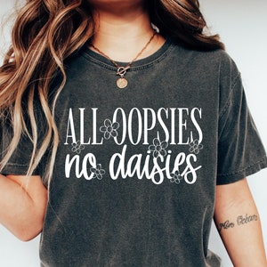 May include: A dark gray t-shirt with the text "ALL OOPSIES no daisies" in white lettering with small flower accents.