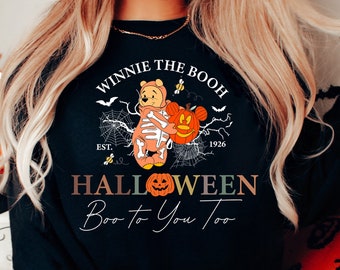 Op de afbeelding: Zwart sweatshirt met een Winnie de Poeh Halloween-ontwerp. Het ontwerp toont Winnie de Poeh verkleed als skelet met een pompoen met Mickey Mouse-oren. De tekst luidt "Winnie de Poeh, Est. 1926, Halloween, Boo to You Too."