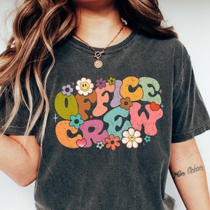 Może przedstawiać: Szary t-shirt z nadrukiem w stylu retro, na którym widnieje napis "Office Crew" w kolorowych literach otoczonych kwiatami.