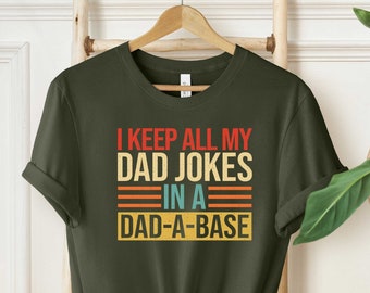 May include: A green t-shirt with a retro-style graphic that says "I keep all my dad jokes in a dad-a-base".