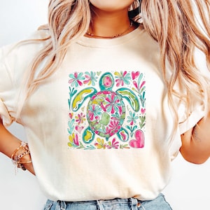May include: A white t-shirt with a colorful graphic of a sea turtle surrounded by flowers and hearts.