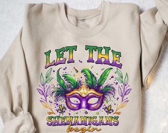 May include: A beige sweatshirt with a purple, green, and gold Mardi Gras mask graphic and the text "Let the Shenanigans begin".