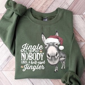 May include: Green sweatshirt with the text "Jingle all the way, nobody likes a half assed Jingler" and a graphic of a donkey wearing a Santa hat. The sleeves are cuffed.