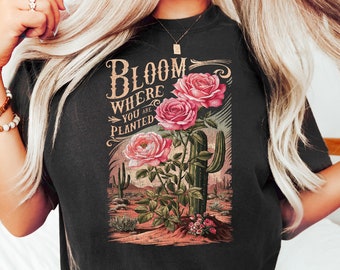 May include: Black t-shirt with a vintage-style graphic featuring pink roses, a cactus, and the text "Bloom Where You Are Planted".