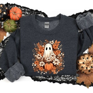 May include: A dark gray sweatshirt with a white ghost surrounded by orange and white flowers. The ghost has a friendly face and is wearing a white flower crown. The sweatshirt is perfect for Halloween.