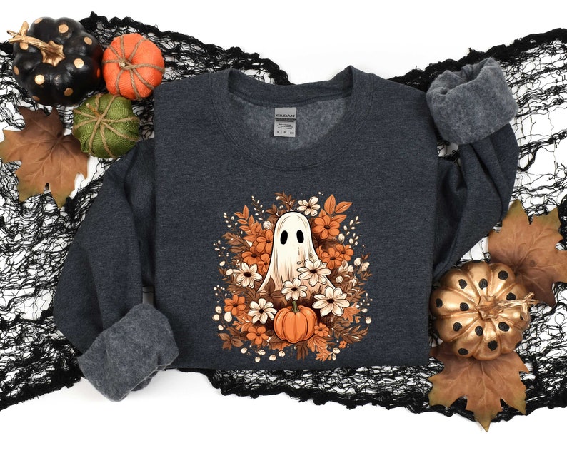 May include: A dark gray sweatshirt with a white ghost surrounded by orange and white flowers. The ghost has a friendly face and is wearing a white flower crown. The sweatshirt is perfect for Halloween.