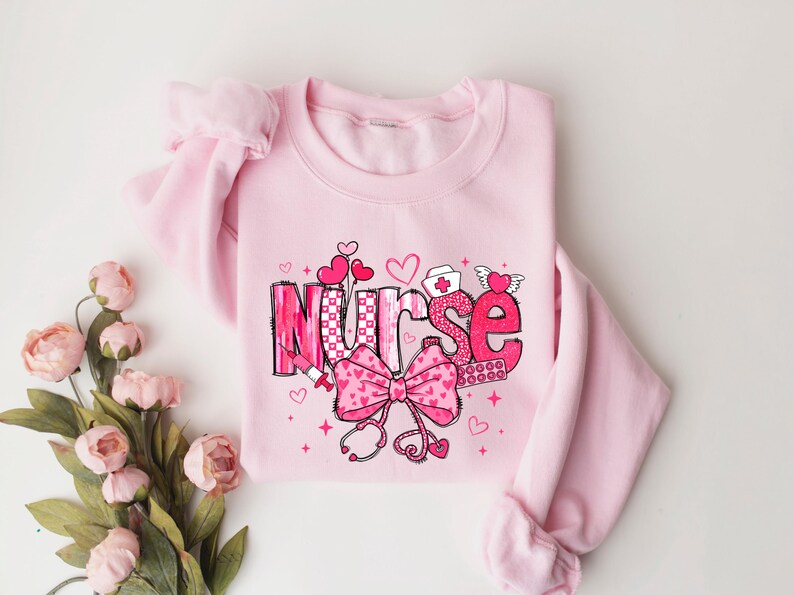 Peut inclure: Sweat-shirt rose avec un motif graphique du mot "Nurse" en rose et blanc avec des c&oelig;urs, un n&oelig;ud et des symboles m&eacute;dicaux.