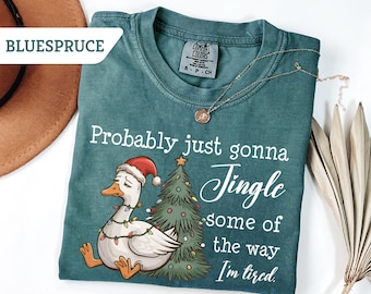 May include: Teal Comfort Colors t-shirt with a Christmas-themed graphic. The design features a goose wearing a Santa hat and Christmas lights, with a Christmas tree. Text reads "Probably just gonna Jingle some of the way I'm tired."