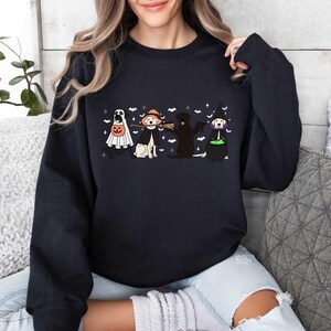 May include: Black sweatshirt with a Halloween-themed design featuring four dogs dressed up in costumes. The dogs are a ghost, a witch, a black lab, and a golden retriever. The text on the sweatshirt says "Boo!"