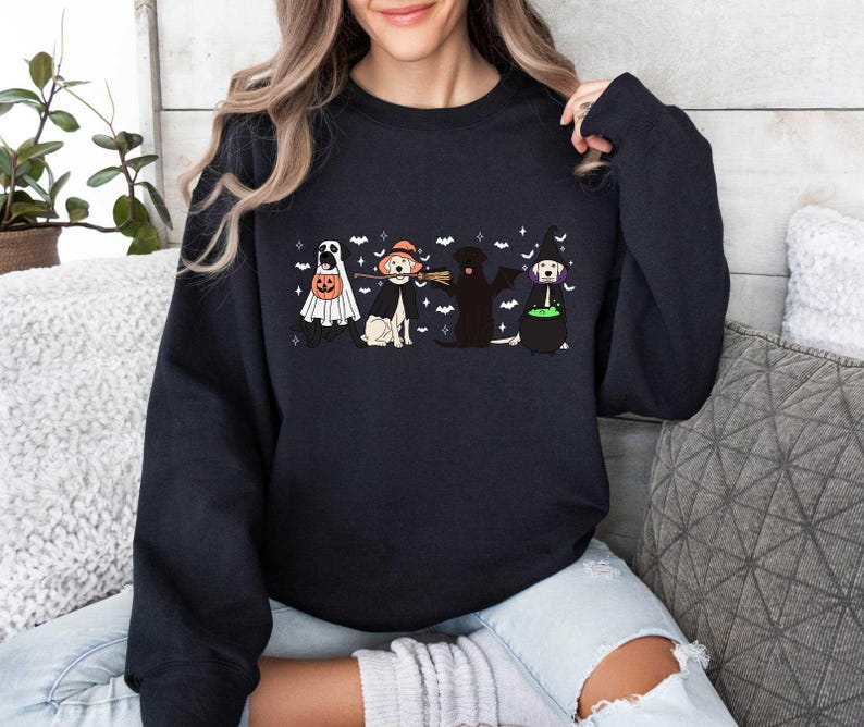 May include: Black sweatshirt with a Halloween-themed design featuring four dogs dressed up in costumes. The dogs are a ghost, a witch, a black lab, and a golden retriever. The text on the sweatshirt says "Boo!"