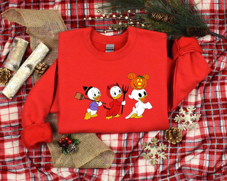 May include: Red sweatshirt featuring a graphic of three cartoon ducks dressed in Halloween costumes. The ducks are wearing a witch hat, devil horns, and a ghost costume with a jack-o-lantern on their head.