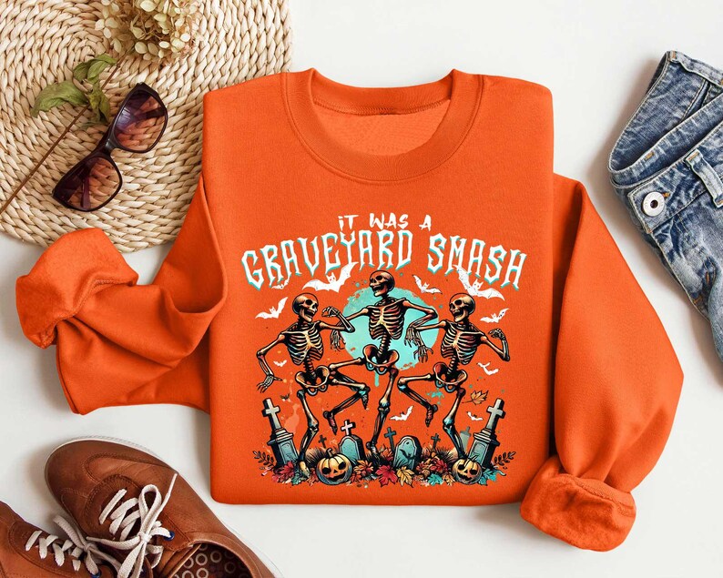 May include: Orange sweatshirt with a graphic of three skeletons dancing and the text "It was a Graveyard Smash".