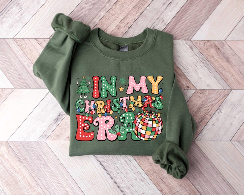 Op de afbeelding: Groen sweatshirt met een feestelijk ontwerp dat "In My Christmas Era" zegt met een discobal en een kerstboom.