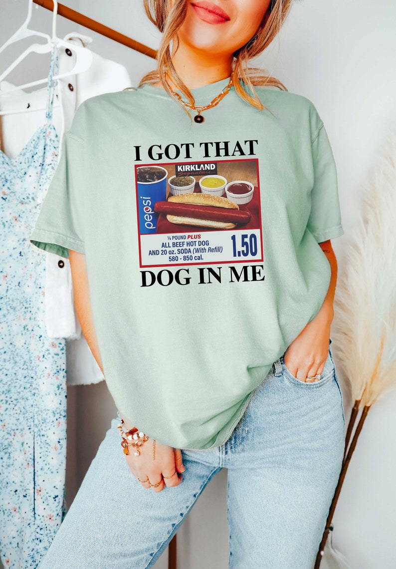 May include: A light green t-shirt with the text "I GOT THAT KIRKLAND" and a vintage-style advertisement for a hot dog meal with a Pepsi can, a hot dog, and condiments. The ad text reads "1/4 POUND PLUS ALL BEEF HOT DOG AND 20 oz. SODA (With Refill) 580-850 cal. 1.50 DOG IN ME."