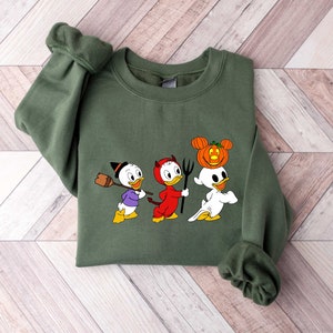 May include: A green sweatshirt with a Halloween-themed design featuring three cartoon ducks dressed as a witch, devil, and ghost. The ghost duck is wearing a pumpkin on its head.