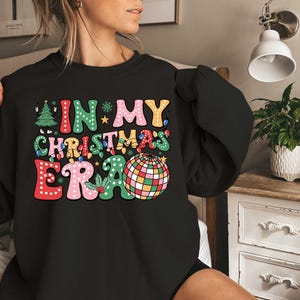 Op de afbeelding: Zwart sweatshirt met een kleurrijke afbeelding die "In My Christmas Era" zegt met een discobal afbeelding.