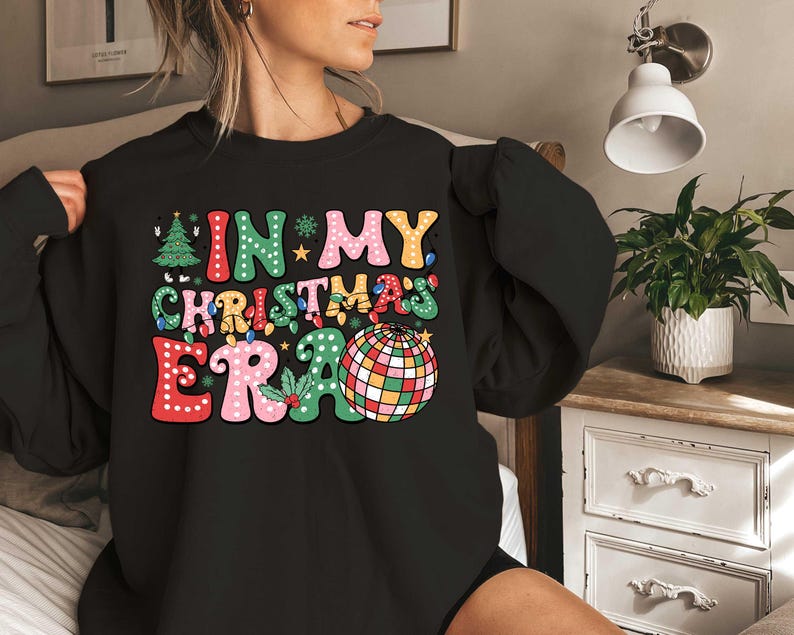 Op de afbeelding: Zwart sweatshirt met een kleurrijke afbeelding die "In My Christmas Era" zegt met een discobal afbeelding.
