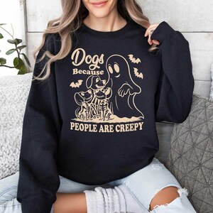 Puede incluir: Sudadera negra con un dise&ntilde;o gr&aacute;fico blanco que representa un fantasma y tres perros. El texto dice "Dogs Because People Are Creepy".