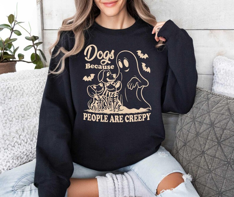 Puede incluir: Sudadera negra con un dise&ntilde;o gr&aacute;fico blanco que representa un fantasma y tres perros. El texto dice "Dogs Because People Are Creepy".