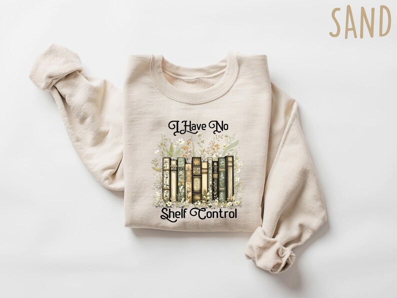 K&ouml;nnte beinhalten: Ein beiger Pullover mit dem Aufdruck "I Have No Shelf Control" auf der Vorderseite. Der Text ist von einer Grafik mit einem Stapel B&uuml;cher mit floralen Akzenten umgeben.
