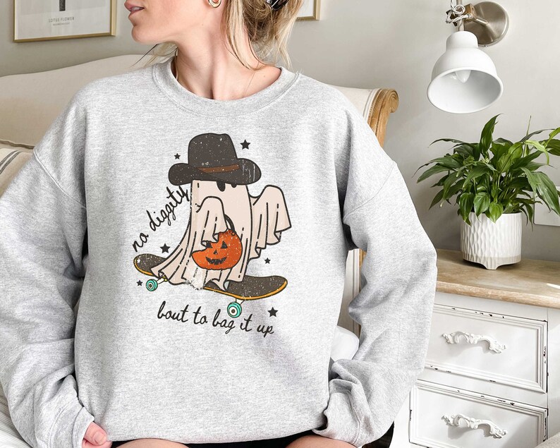 May include: A gray sweatshirt with a graphic of a ghost wearing a hat and holding a pumpkin. The ghost is skateboarding and the text "no diggity bout to bag it up" is printed below the ghost.