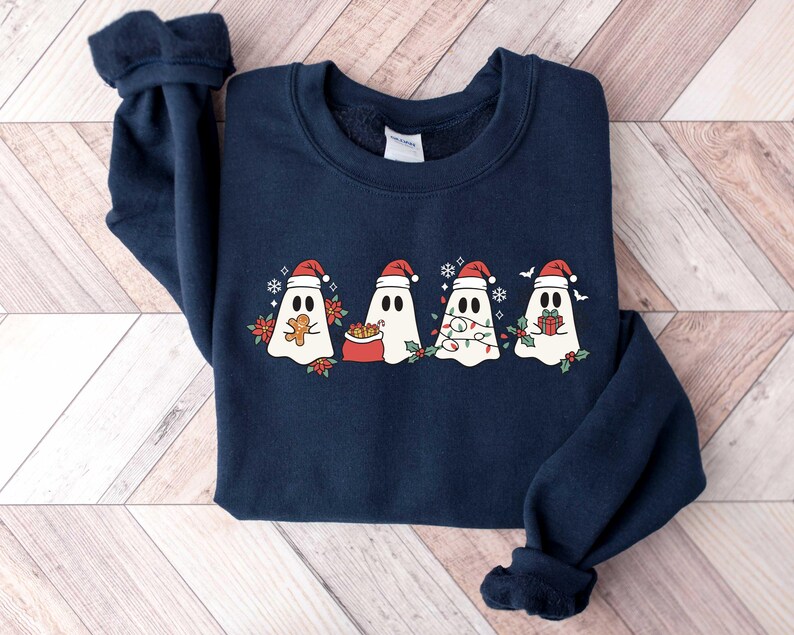 Op de afbeelding: Een donkerblauw sweatshirt met een kerstthema met vier geesten die een kerstmanmuts dragen. De geesten houden geschenken, snoepstokken en lampjes vast.