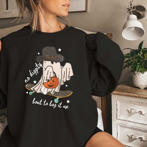 May include: Black sweatshirt with a graphic of a ghost skateboarding and holding a pumpkin. The text on the sweatshirt reads "no digity bout to bag it up".