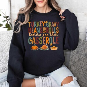May include: Black sweatshirt with a Thanksgiving-themed graphic that says "Turkey Gravy Beans and Rolls lemme see that Casserole". The graphic features a pumpkin, a turkey, and a pie.