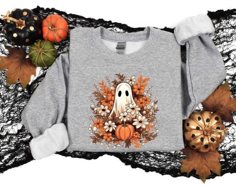 May include: A gray sweatshirt with a white ghost surrounded by orange, brown, and white flowers. The ghost is smiling and has a small pumpkin in its hand.
