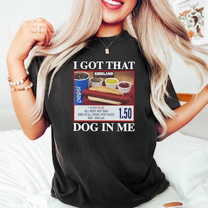May include: A black t-shirt with the text "I GOT THAT KIRKLAND" and a picture of a hot dog meal with a Pepsi, a hot dog, and condiments. The text "1.50" and "DOG IN ME" are also on the shirt.