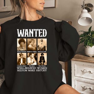 May include: Black sweatshirt with a white graphic print that says "WANTED" and features images of six women with their names listed below. The text below the images reads "Well-behaved women seldom make history."