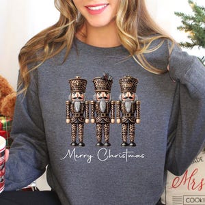 May include: A gray sweatshirt with a graphic of three nutcracker figurines wearing leopard print outfits. The text "Merry Christmas" is written below the figurines.