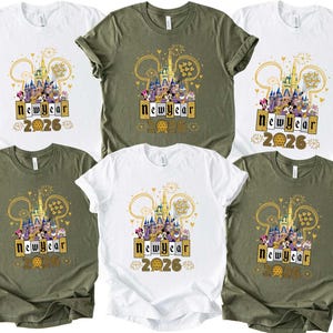 May include: White and olive green t-shirts with a graphic design featuring a castle, Mickey Mouse ears, and the text "New Year 2026". The design is in gold, purple, and yellow.