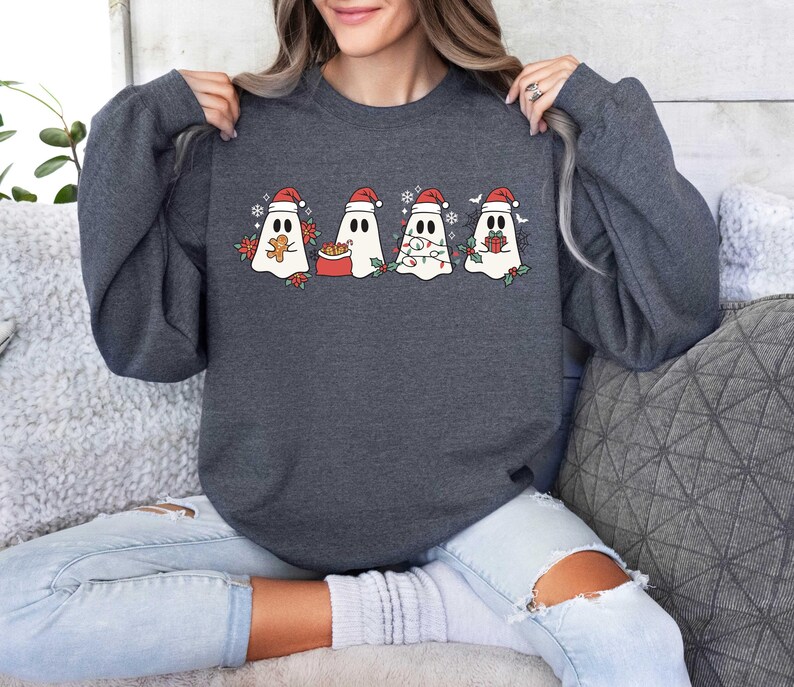 Op de afbeelding: Een donkergrijs sweatshirt met een feestelijk ontwerp met vier geesten die kerstmanmutsen dragen. De geesten houden een peperkoekman, een cadeau, een lichtsnoer en een snoepstok.