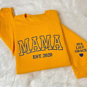 May include: Yellow sweatshirt with blue text that reads "MAMA EST. 2020" and "AVA LILY GRACE" with a blue heart on the sleeve.