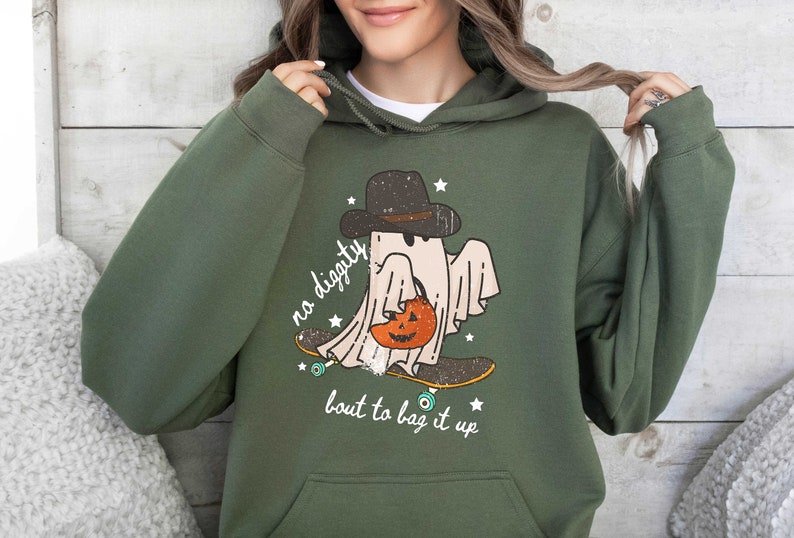 May include: Green hooded sweatshirt with a graphic of a ghost wearing a hat and holding a pumpkin. The ghost is skateboarding and the text "no diggity bout to bag it up" is printed below the ghost.