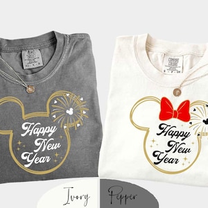May include: Two t-shirts, one grey and one white, with a gold outline of Mickey Mouse ears and "Happy New Year" text. The white shirt has a red bow. Both shirts have a gold necklace.