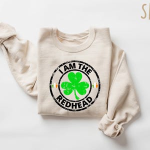 Puede incluir: Una sudadera de color arena con un gr&aacute;fico circular negro que dice "Soy el pelirrojo" con un tr&eacute;bol verde dentro del c&iacute;rculo.