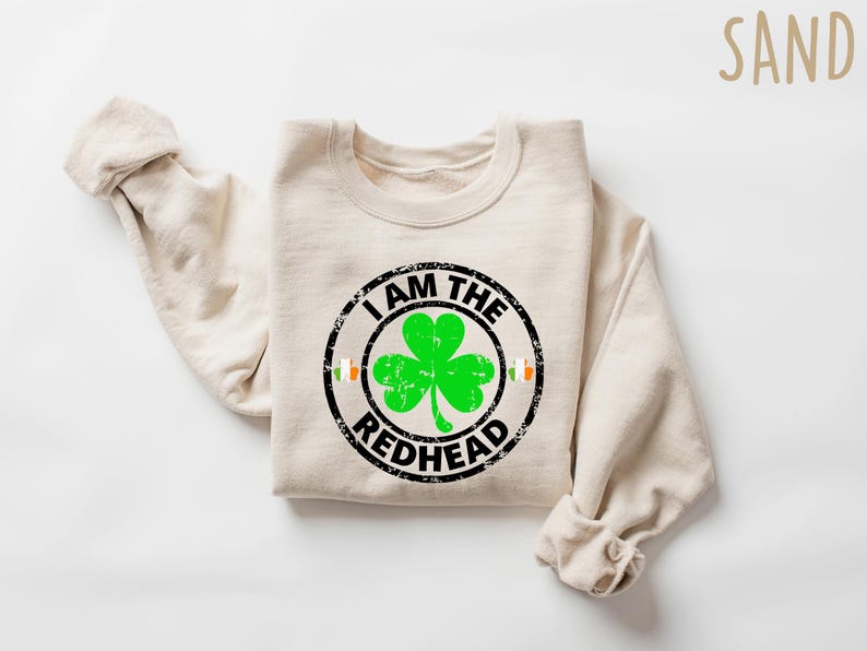 Puede incluir: Una sudadera de color arena con un gr&aacute;fico circular negro que dice "Soy el pelirrojo" con un tr&eacute;bol verde dentro del c&iacute;rculo.