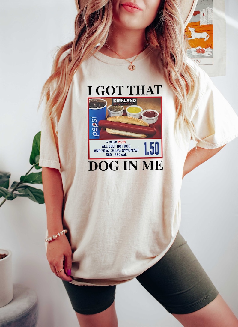 May include: A white t-shirt with the text "I GOT THAT" and a picture of a Kirkland Signature hot dog meal with a Pepsi. The text "DOG IN ME" is below the picture.