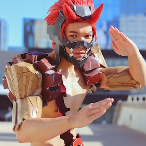 May include: A person wearing a red and black costume with a red and white belt. The costume features a mask with a sharp, angular design. The person is posing with their arms raised.