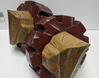 May include: Two brown and tan gears with a rough, textured surface. The gears are connected and have a worn, distressed look.