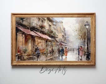 May include: A watercolor painting of a Parisian street scene with a shop on the left side of the street and people walking in the rain. The buildings are painted in shades of beige and brown, and the street is paved with cobblestones. The painting is framed in a gold frame.