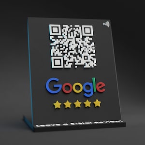 May include: A black sign with a white QR code, the word "Google" in colorful letters, and five yellow stars. The sign says "Leave a Google Review".