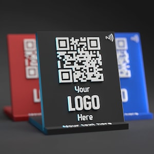 Peut inclure: Un support noir avec un code QR blanc, le texte "Your LOGO Here" et un petit symbole wifi bleu. Le support est sur une surface grise.