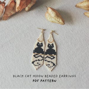 Może przedstawiać: Para kolczyków z koralików z czarnym motywem kota na kremowym tle. Kolczyki mają złote wierzchy i frędzle na dole. Tekst "BLACK CAT MOON BEADED EARRINGS PDF PATTERN" znajduje się na dole.