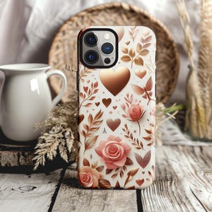 May include: A white phone case with a floral design featuring roses, hearts, and leaves in shades of pink and copper. The case has a glossy finish and a camera cutout. The design is set against a white background.